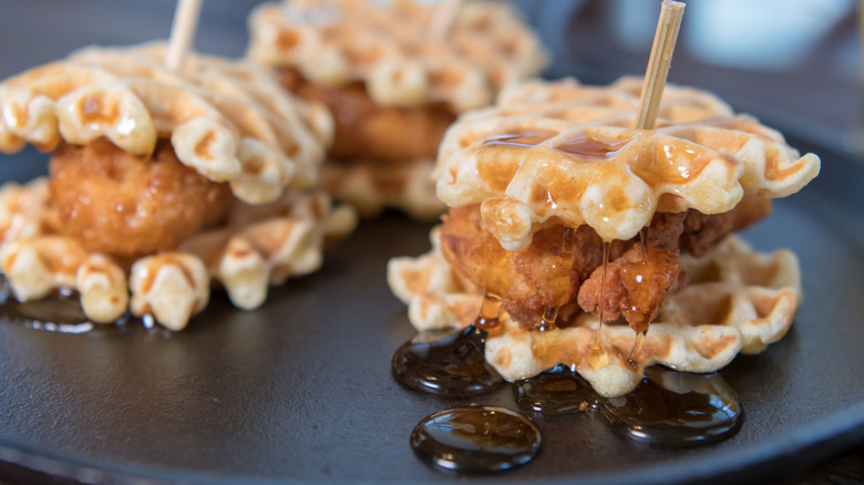 Three chicken and waffles sandwiches on a black serving platter