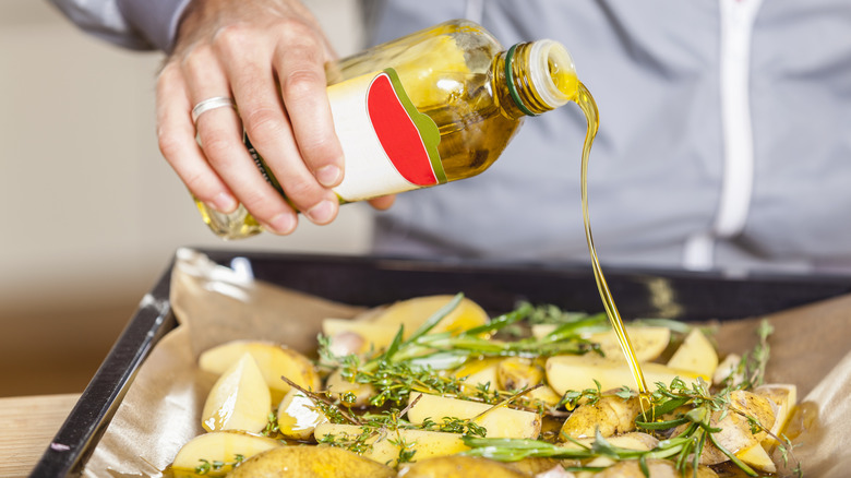 person Pouring oil over potatoes and herbs