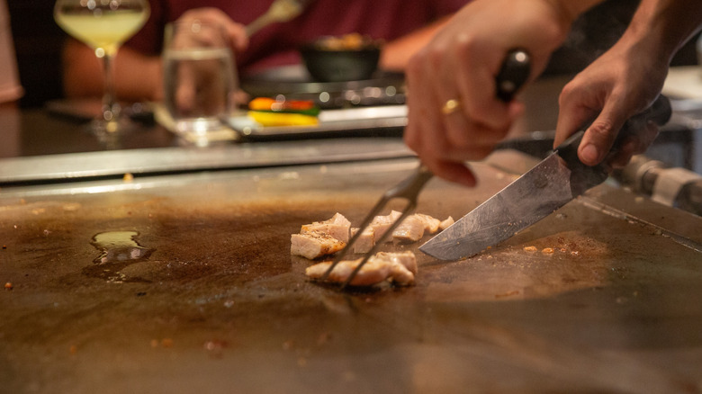 Slicing hibachi chicken on a griddle.