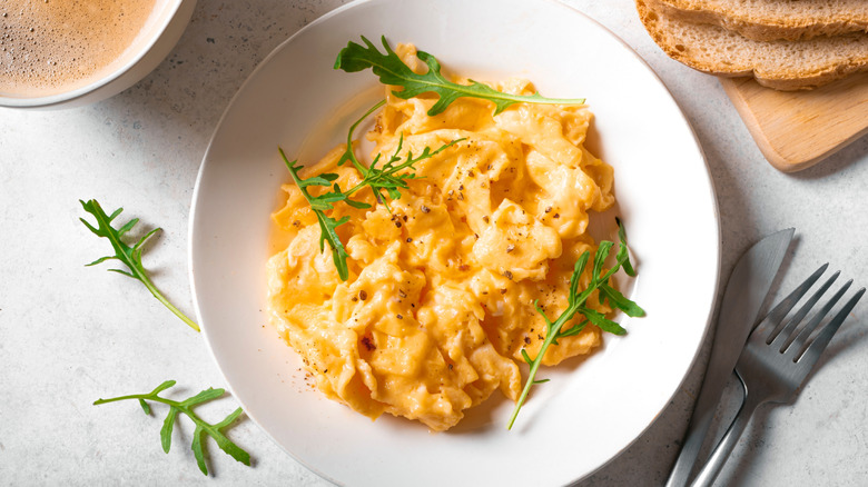 A plate of scrambled eggs with herbs, a cup of coffee, and sliced bread.