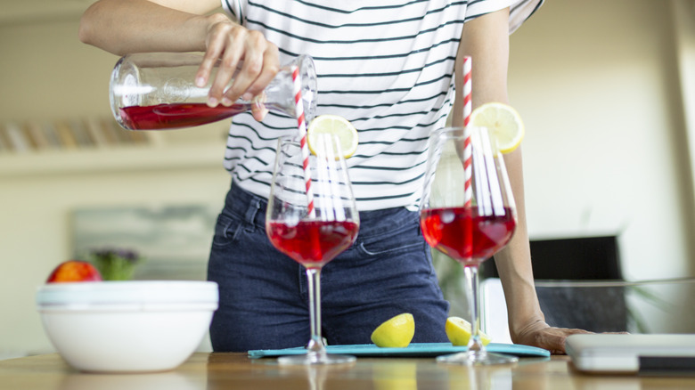 Closeup of a hand pouring red juice into cocktails