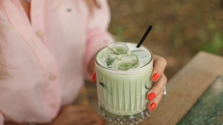 woman with orange nails drinks matcha