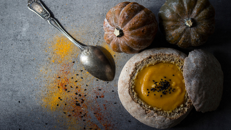 Soup in a bread bowl next to two acorn squashes