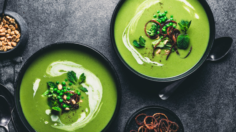 Two bowls of green soup with basil garnish