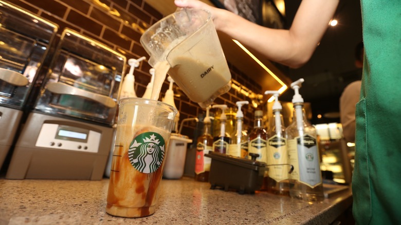 Starbucks barista pouring milk into an iced caramel drink