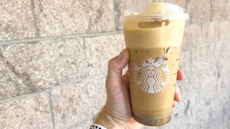 Hand holding a Starbucks iced drink with foam