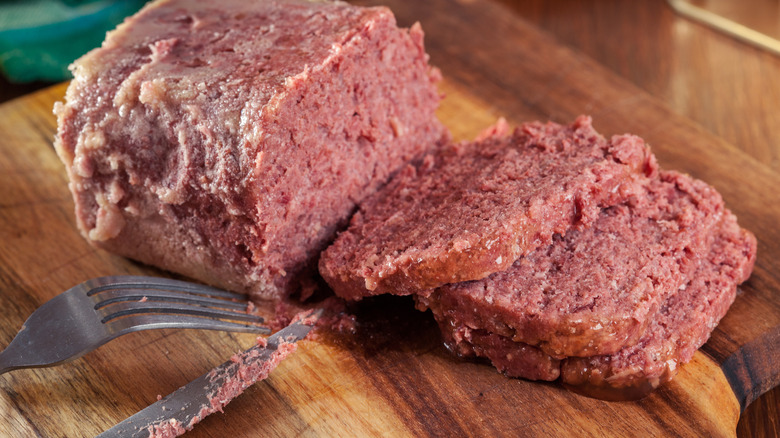 Canned corned beef sliced on a wooden cutting board