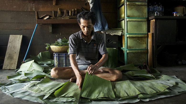 man cutting banana leaves for tempeh