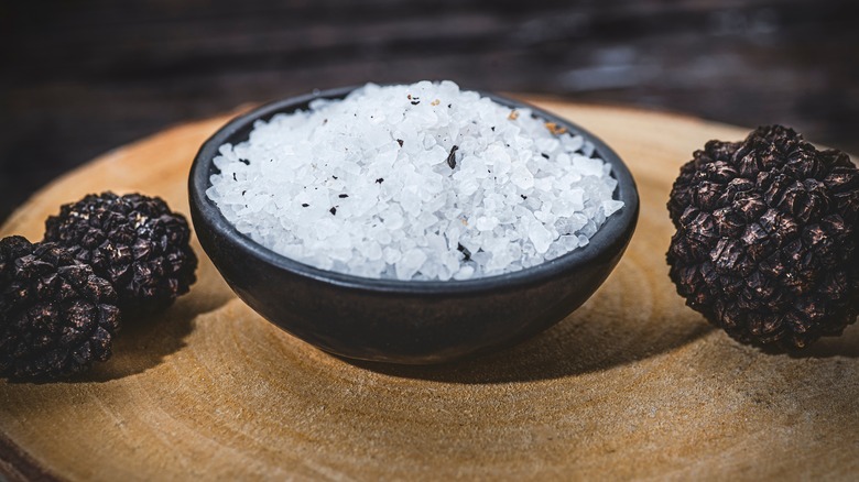 Black truffle salt in a rustic bowl surrounded by fresh whole truffles