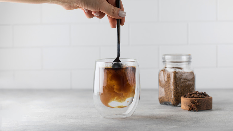 woman stirring instant coffee into a glass with hot water