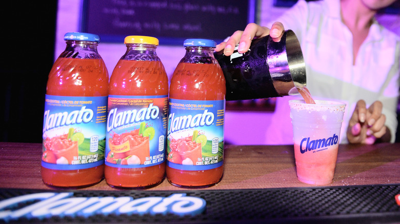 cocktail being poured next to bottles of Clamato