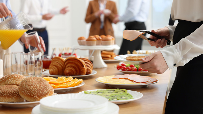 Person moving down buffet line with buns, meat, cheeses