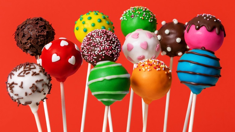 Twelve multi-colored decorated cake pops on a red background