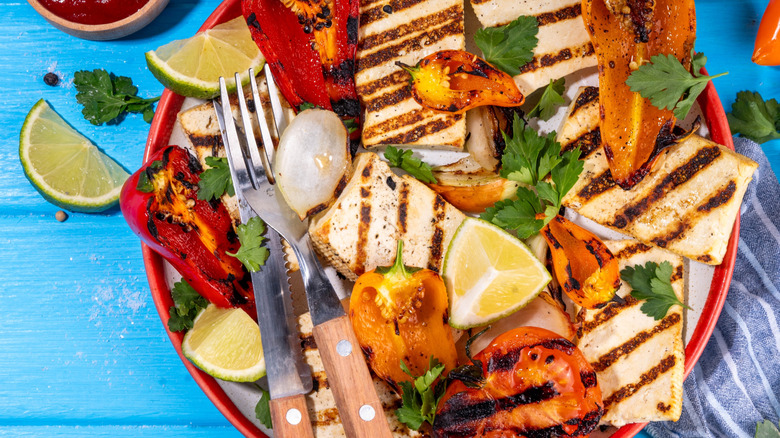 A plate of grilled tofu, peppers, and limes on a blue background