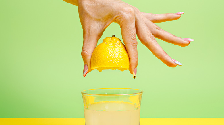 Hand squeezing lemon wedge into glass full of juice