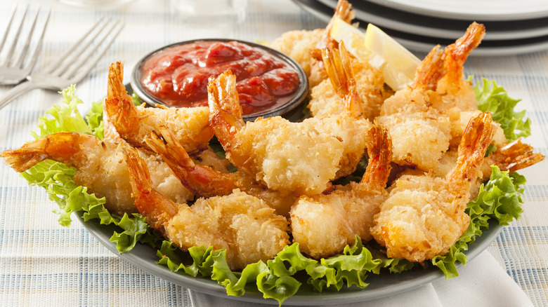 plate of fried coconut shrimp with dipping sauce and lemon wedges