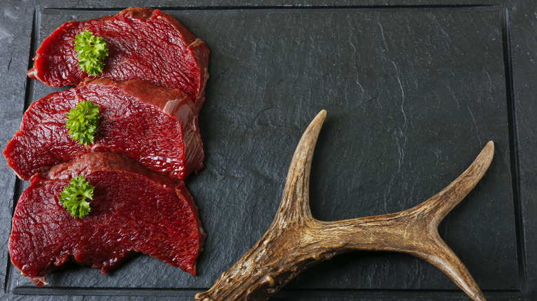 Three venison steaks on a cutting board beside an antler