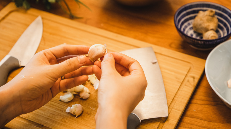 Hands peeling garlic over cutting board