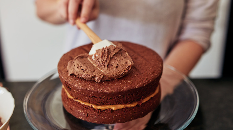 Hands, spatula spreading chocolate icing on cake