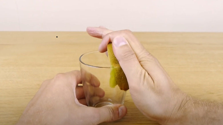 hands peeling kiwi with glass