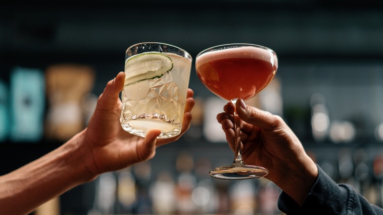 Two people cheersing cocktails in different-shaped glasses