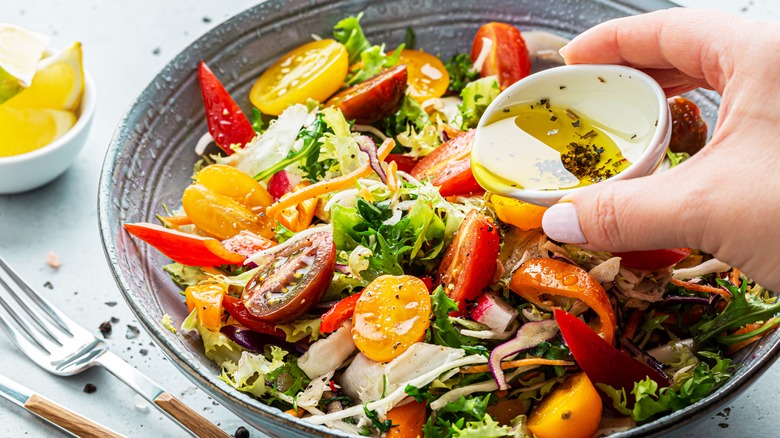 Hand pouring salad dressing on salad