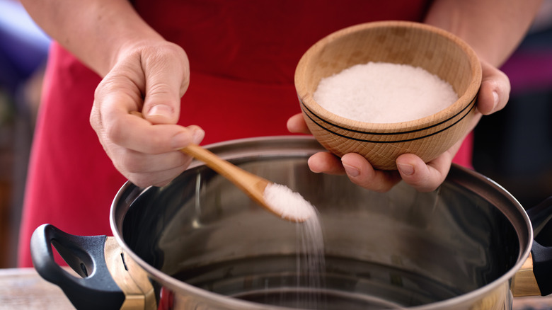 person salting pot of water