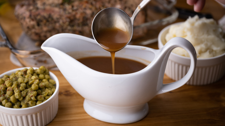 A gravy boat with a spoon beside peas and mashed potatoes