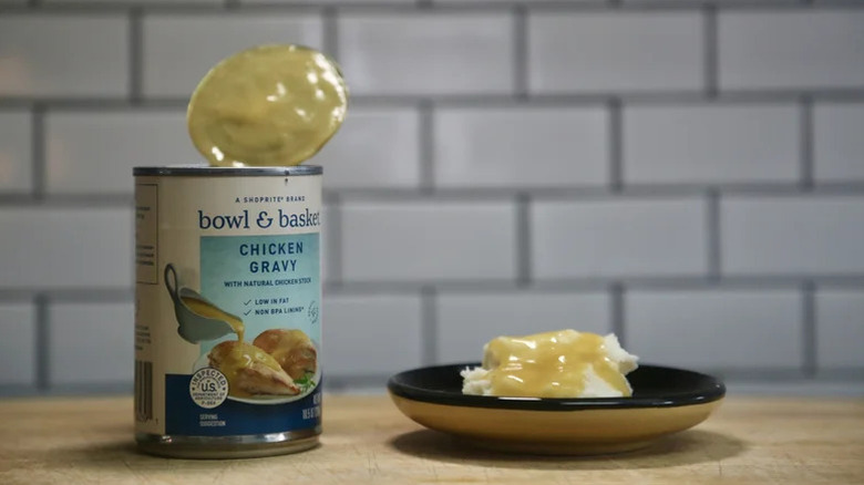 A can of Bowl & Basket Chicken Gravy beside a plate of mashed potatoes and gravt