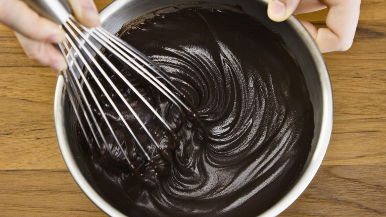 A hand whisking a bowl of chocolate ganache