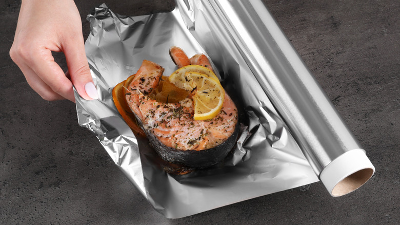 Someone wrapping leftover salmon in aluminum foil.