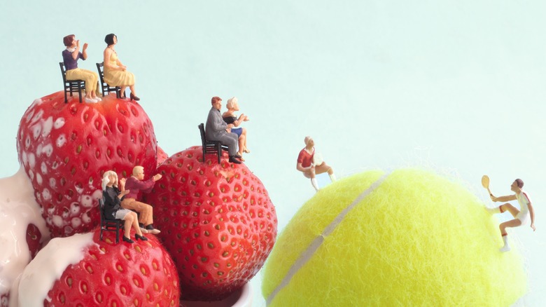 Miniatures on strawberries watch tennis match  