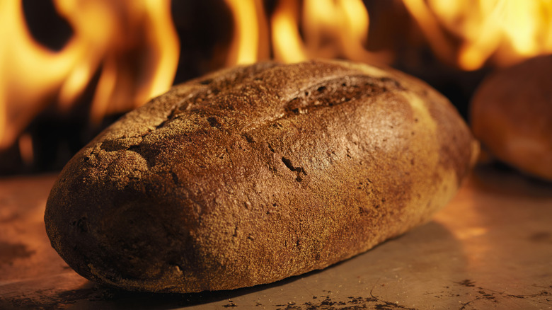 A loaf of pumpernickel bread in front of a firey oven