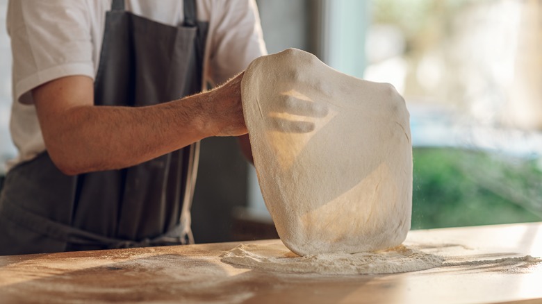 person stretching pizza dough