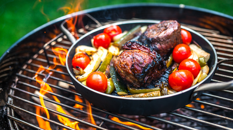 a pan of meat and veggies cooking on a grill