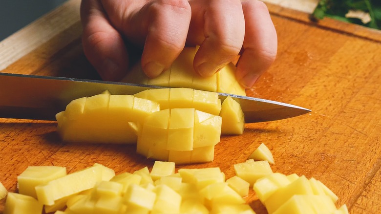 Knife cubing potato on board