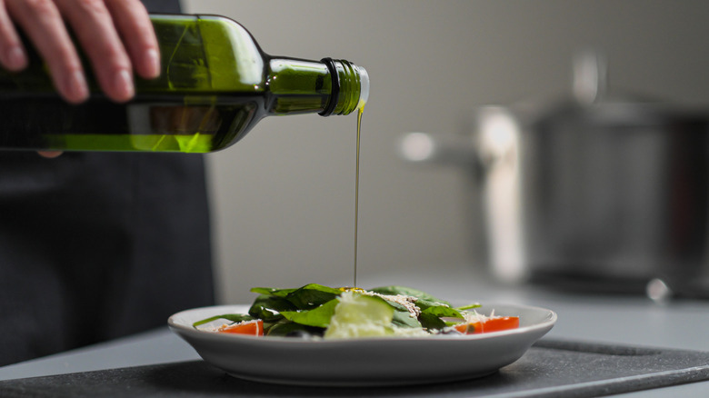 Hand pouring olive oil on salad