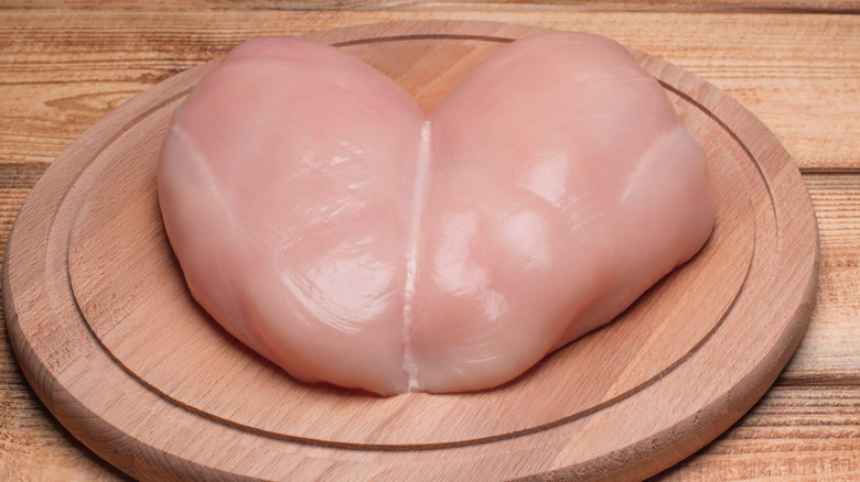 Butterflied raw chicken breast wooden chopping board