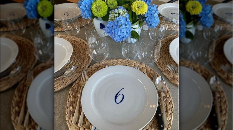 White plate with the number 6 setting on a table with glasses and flowers