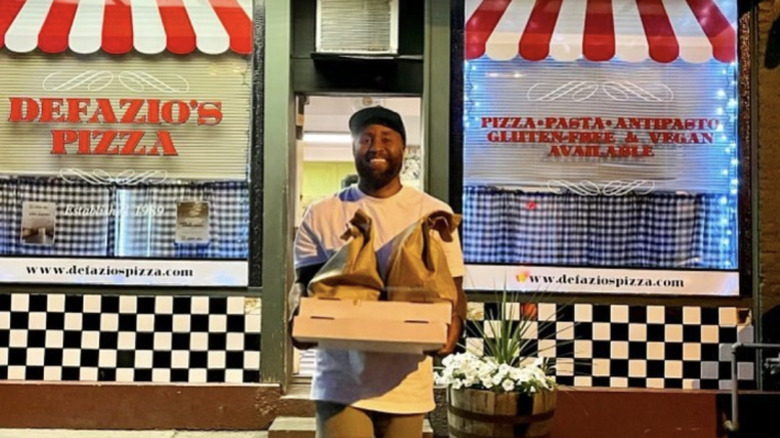 A man holding to-go bags and a pizza box in front of DeFazio's Wood Fire Pizza
