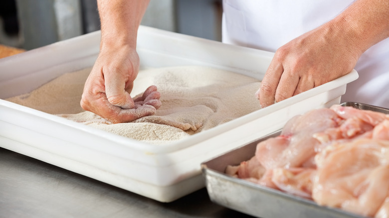 hands dredging chicken in flour