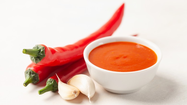 a bowl of sriracha chili sauce next to a red pepper and clove of garlic