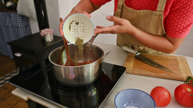 Home cook adding spices to a pot to prepare a meal