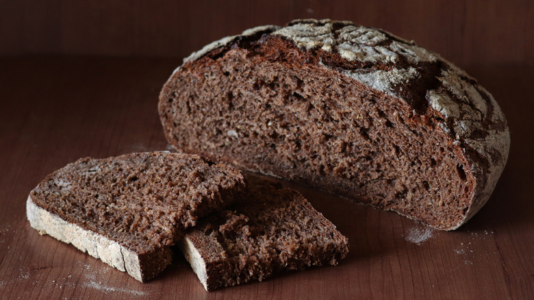 Dark rye artisan loaf cut open on wooden board