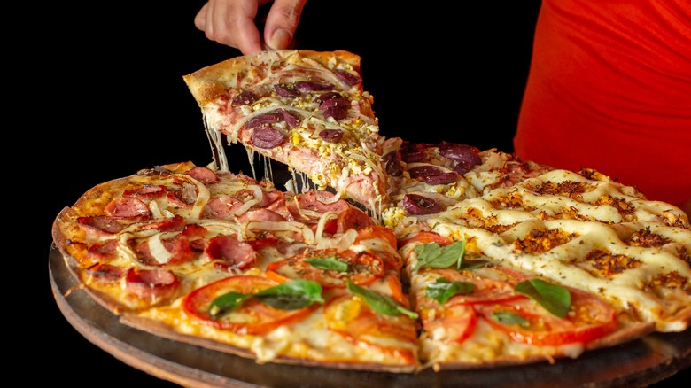 Hand slicing pizza with different toppings