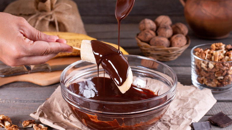 hand spooning chocolate sauce over a banana