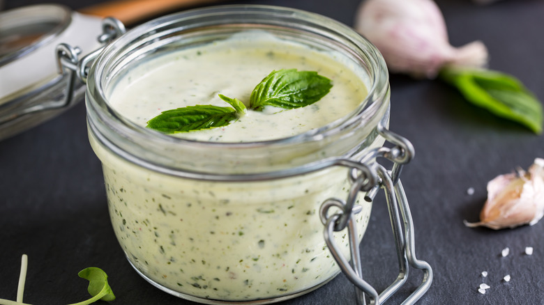 yogurt-based dressing in a mason jar with fresh garlic and basil in the background