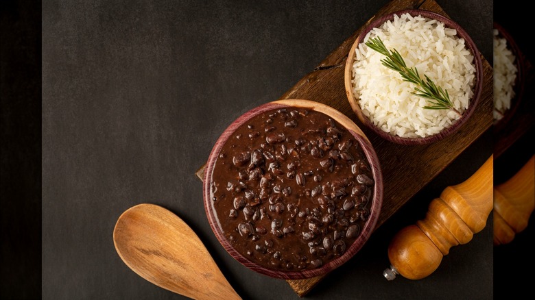 bowl of black beans and bowl of white rice on a wooden cutting board