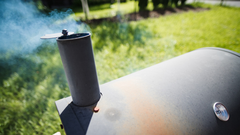 Smoke rises out of the top of a smoker in a backyard