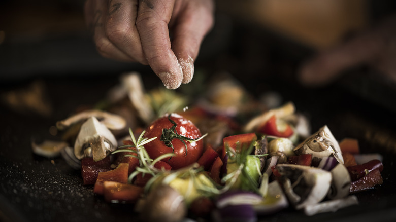 hand sprinkling veggies with seasoning